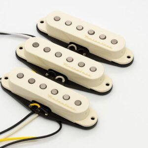 Close-up studio photo of three Fender Vintage Noiseless Stratocaster pickups in aged white, showing the stacked-coil single-coil design with pole pieces, gold “Noiseless” lettering, black bases, and color-coded wiring on a white background.