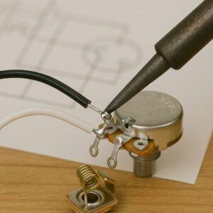 Close-up of soldering wires to a pot/output jack, with a wiring diagram faintly in the background.