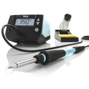 A Weller WE1010 soldering station set with digital temperature display, matching soldering iron, coiled metal iron holder, and yellow cleaning sponge on a white reflective surface.