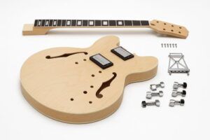 Unfinished ES-style hollow-body DIY guitar kit with maple body, F-holes, maple neck, pickups, bridge, and hardware laid out on a white background.