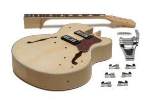Unfinished ES-style hollow-body DIY guitar kit with natural wood body, tortoise-style pickguard, dual humbuckers, maple neck, and full hardware including a vibrato tailpiece laid out on a white background.