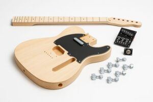 Unfinished Tele-style DIY guitar kit laid out on a white background, featuring a natural wood body with black pickguard, a maple neck, pre-wired control plate, output jack, and chrome tuning machines.