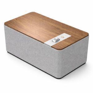 Modern rectangular Bluetooth speaker with a light-gray fabric body, warm walnut wood top, and brushed aluminum control knob, photographed on a clean white background.